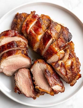 A bacon-wrapped pork tenderloin in a roasting pan, seasoned with garlic, brown sugar, and rosemary, ready to be roasted in the oven.