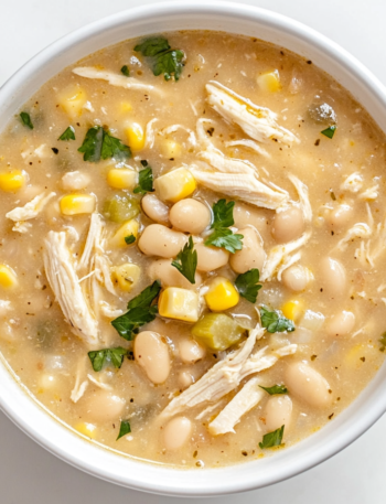 A large pot of creamy white chicken chili simmering on the stove, filled with tender shredded chicken, beans, corn, and a blend of spices.